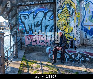 Senior Elderly main drinks a beer next to graffiti-covered wall in the  James Simon Park, Mitte, Berlin Stock Photo