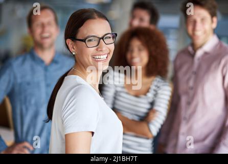 Our office works runs great staff. Beautiful businesswoman smiling with friendly coworkers in the background. Stock Photo