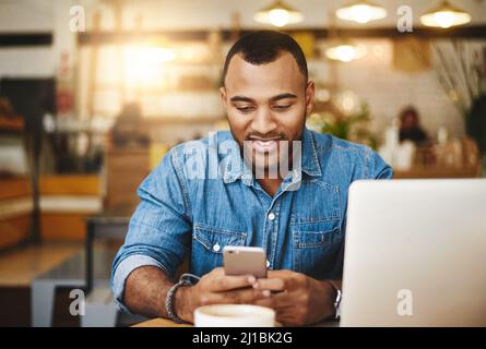 Taking a break with his connections. Shot of a handsome young woman using a cellphone and laptop in a cafe. Stock Photo