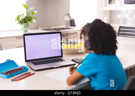 Rear view of hispanic boy attending online class through laptop at home Stock Photo