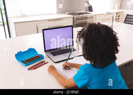 Hispanic boy writing while attending online classes through laptop at home Stock Photo