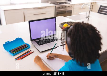 Hispanic boy attending online classes through laptop while sitting at dining table Stock Photo