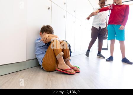 Multiracial elementary schoolboys bullying male classmate wearing ...