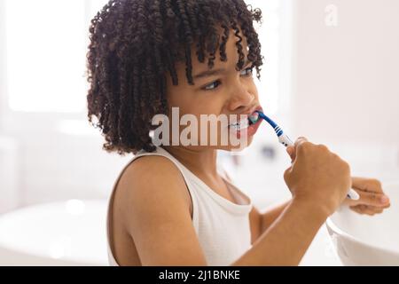 Cute curly hair hispanic boy brushing teeth in bathroom at home Stock Photo