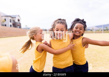 Cheerful multiracial elementary school girls in sports uniform on ground during soccer practice Stock Photo