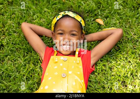 High angle portrait of smiling african american girl lying with hands behind head in backyard Stock Photo