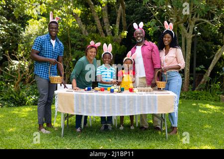 Happy african american multigenerational family in bunny ears with easter eggs in backyard Stock Photo