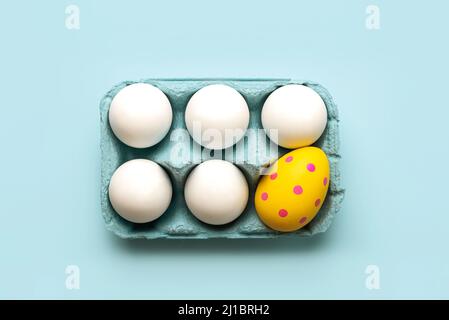 Happy Easter. Top view of chicken eggs and easter painted egg in an open blue cardboard box over blue background Stock Photo