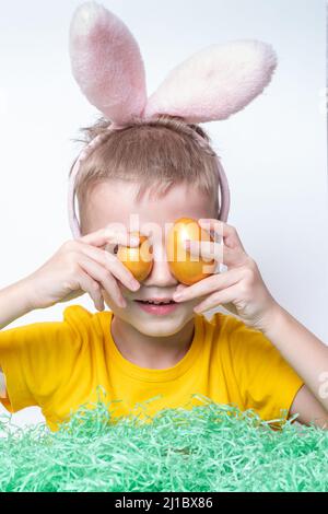 Portrait of a little blond boy covering his eyes with colorful eggs, close-up, vertical frame. Easter family holiday. The child has fun and celebrates Stock Photo