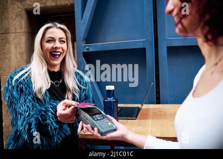 Female customer making a contactless payment with a credit card in a coffee shop. Stock Photo