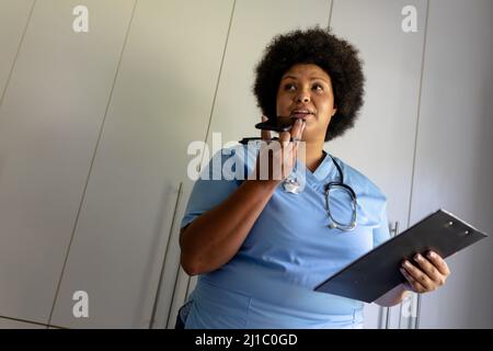 African american mid adult female nurse talking on call while holding clipboard Stock Photo
