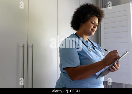 Smiling african american mid adult female nurse writing on clipboard in hospital Stock Photo