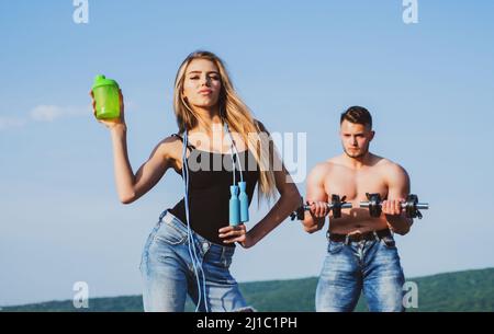 Slim female fitness trainer with protein shaker. Man and girl with protein shake bottle and skipping rope. Smiling young woman and personal couple Stock Photo