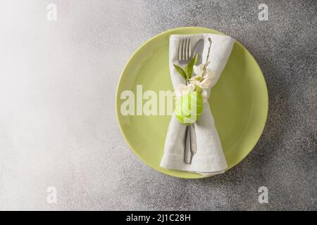 Easter table setting with green plate and egg, spring blossom flowers on gray background. View from above. Copy space. Greeting card. Stock Photo