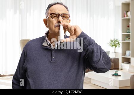 Mature man using a nasal spray at home inside a living room Stock Photo