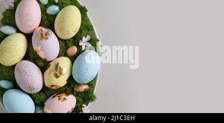 Easter composition in plate with rabbit, moss, flowers and craft eggs decorated gold foil on gray background. Greeting card. Concept Easter eggs hunt. Stock Photo