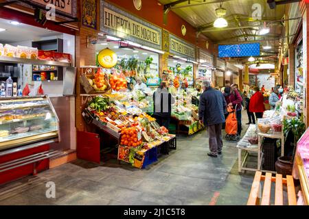 Shoppers pass by stalls selling produce and meats inside the Triana Market or Mercado de Triana in the Andalusian city of Seville, Spain. Stock Photo