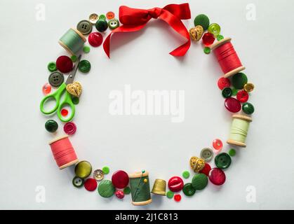 Wreath made of buttons, threads, pins, scissors, thimble red, green and gold color. White background. Copy space. Stock Photo