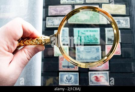 Moscow, Russia, March 2022: Hobby: stamp collecting. Looking at blurred old stamps through a golden magnifying glass. Copy space. Stock Photo