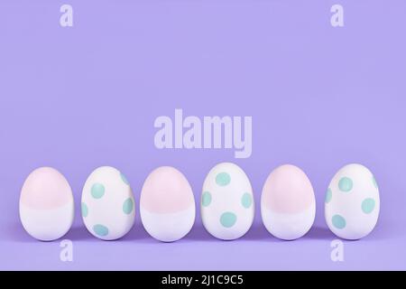 Pastel colored painted mint green and pink easter eggs in a row on violet background Stock Photo