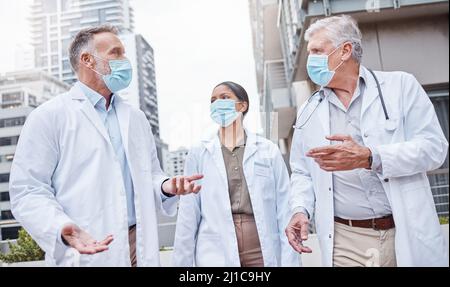Making sure they wear their masks. Shot of a group of doctors talking in the city. Stock Photo