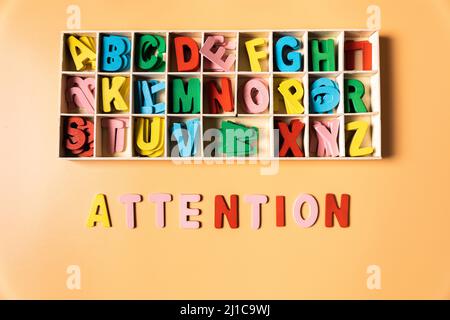 the word attention represented as a concept by wooden color letters, from the perspective of a child, over a background. Stock Photo