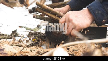 Man cutting wood using stationary circular saw outdoors in winter for kindling close-up Stock Photo