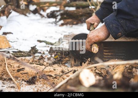 Man cutting wood using stationary circular saw outdoors in winter for kindling close-up Stock Photo
