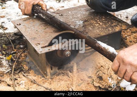 Man cutting wood using stationary circular saw outdoors in winter for kindling close-up Stock Photo