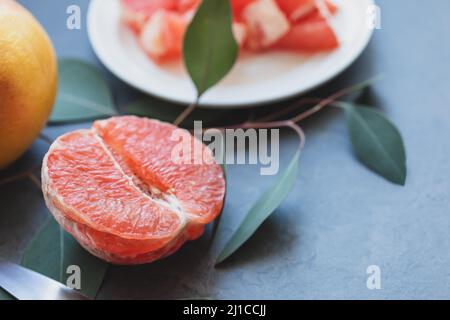 Half a fresh, juicy grapefruit, sliced grapefruit on a plate and a whole grapefruit on a dark marble background with leaves. Citrus fruits is immune b Stock Photo