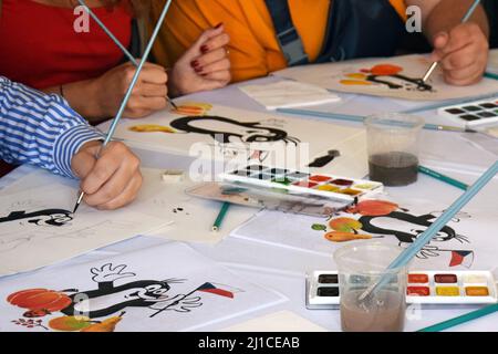 Drawing lesson. People hands use brush and watercolor paints to draw a cartoon character on white paper. RUSSIA, MOSCOW - SEPTEMBER 22, 2018 Stock Photo