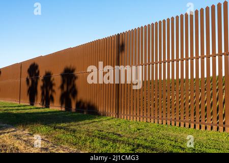 Shadows of palm trees on the  U.S. - Mexico border wall near Brownsville, Texas in late afternoon light.  Viewed from Texas side of the wall. Stock Photo