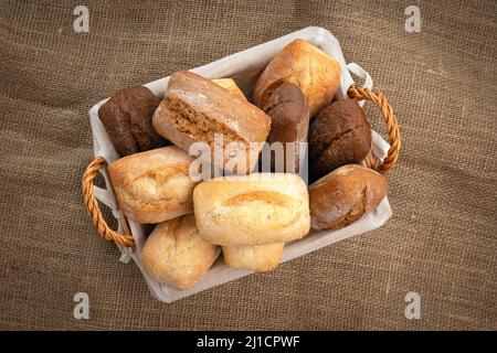 Tasty wheat and rye buns in a wicker basket on a burlap cloth Stock Photo
