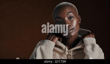 Self confidence is the best outfit to rock. Studio portrait of an attractive young woman wearing a hoodie and posing against a brown background. Stock Photo