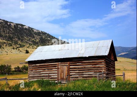 Rustic log cabin, with tin roof, has beautiful backdrop of the Absaroka Mountains in Montana.  Cabin has front door, tin roof and wooden fence. Stock Photo