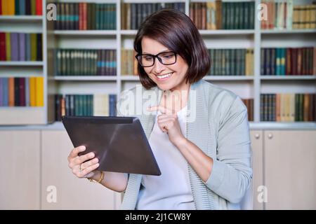 Business smiling mature woman using digital tablet in library office Stock Photo