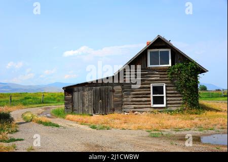 Gravel  road circles rustic log cabin in Happy Valley, Montana.  Galatin Mountains are seen in the distance. Stock Photo