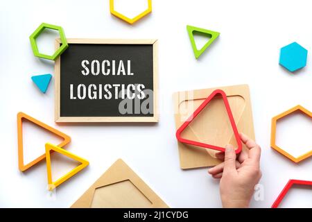 Text Social Logistics on white blackboard. Nested wood triangles and hexagons in rainbow colors. Red triangle in human hand. Stock Photo