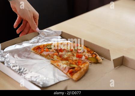 Hand Taking Slice of Pizza from Delivery Box. Copy space on the table. Stock Photo