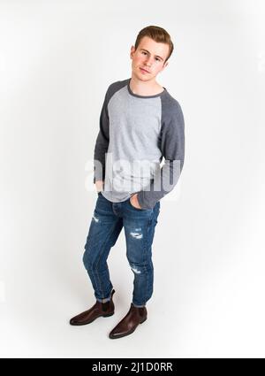 Stylish Handsome Man Posing Sitting On Floor. Handsome Guy. Cool Fashion  Male Model Sitting On Grey Background And Looking At The Camera. Student In  A Studio In Jeans And A Black Sweater.