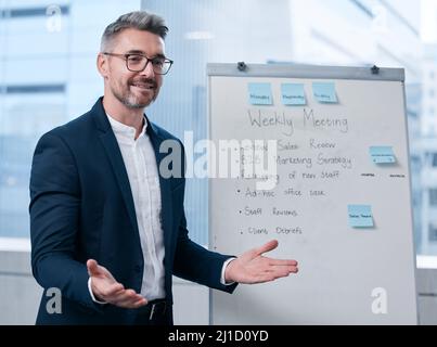 Welcome all to our weekly meeting. Shot of a mature businessman using a whiteboard during a presentation in an office. Stock Photo