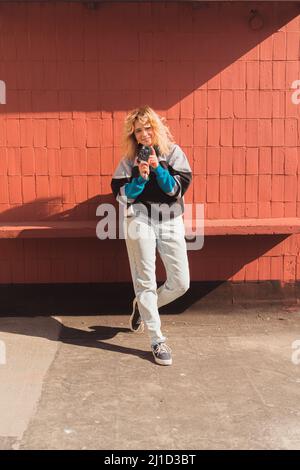 Vertical shot of a beautiful young caucasian blonde woman taking photos with her analog camera over a brick wall. High quality photo Stock Photo