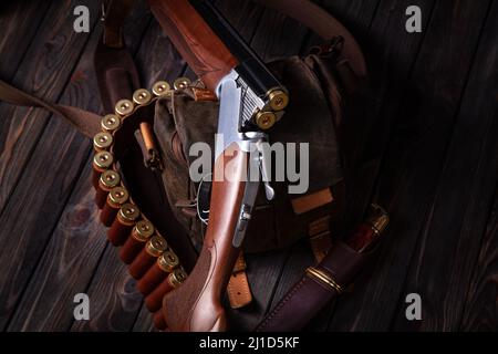 An open hunting rifle with cartridges and a knife in a leather case, lying on the wooden background. Hunting concept Stock Photo