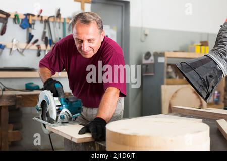 Worker cutting wooden workpiece on an hand electical circular saw Stock Photo