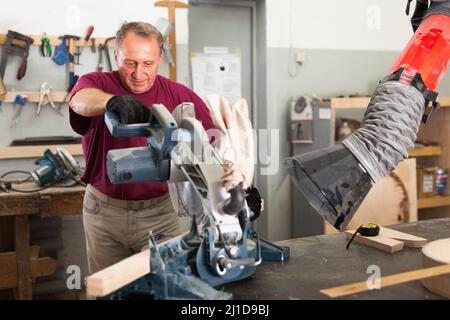 Carpenter cutting a wooden workpiece on an electical circular saw Stock Photo