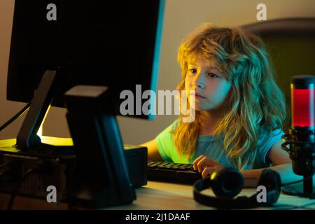 A little boy child uses a desktop at night, a child with computer screen in the room with neon lightning. School, study, online learning concept Stock Photo