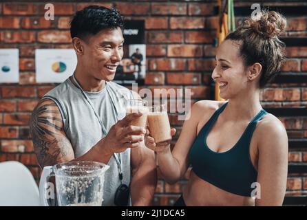 Cheers to a fit and healthy life. Cropped shot of two young sportspeople making a toast with milkshakes while working in a gym. Stock Photo