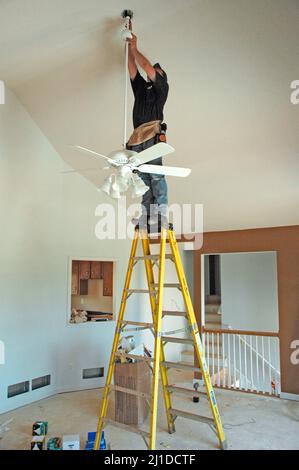 Electrician installing fans, lights and circuit panels and breakers on ladders by hand in new home construction Stock Photo