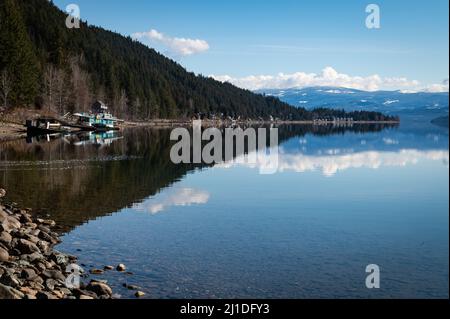 Photo of forest, beach area and colorful houseboat reflected along the north shore of Lake Shuswap in the province's Southern-Interior region. Stock Photo