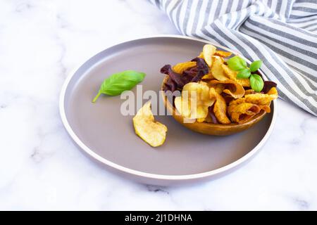 Vegan snacks, multicolored vegetable and fruits chips in wooden bowl , selective focus. Bowl of healthy vegetable chips from beets, sweet potatoes,app Stock Photo